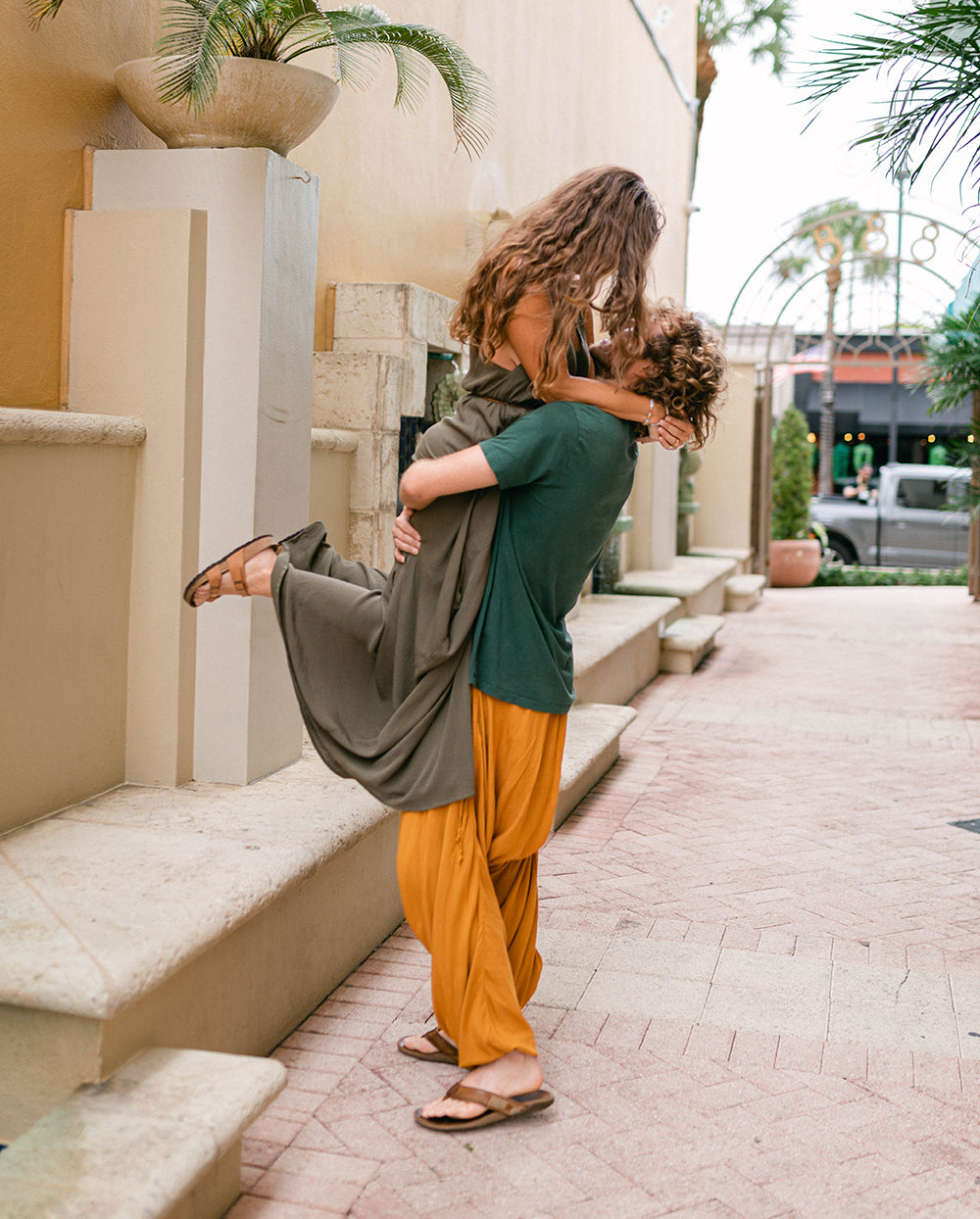 Two people embracing on a sidewalk with palm trees in the background. #color_basil