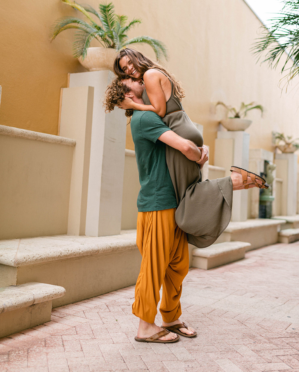 Man lifting a woman in a casual outdoor setting with plants and steps. #color_amber