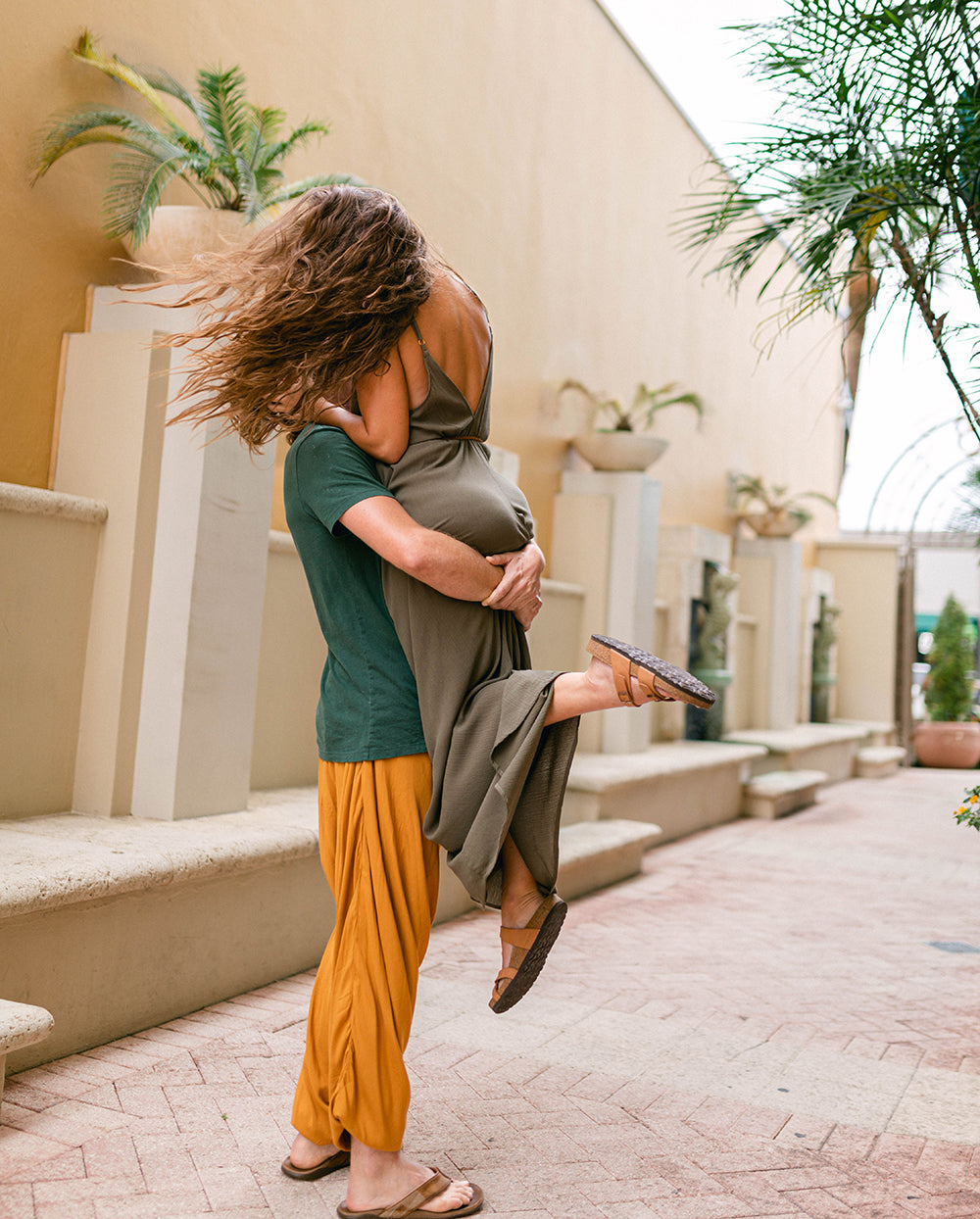 Two people embracing outdoors with a building and plants in the background #color_amber