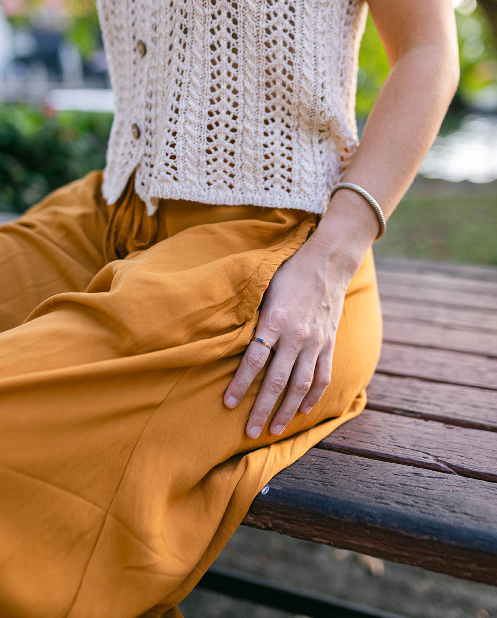 Person wearing mustard yellow pants and a white textured top sitting on a wooden bench. #color_amber
