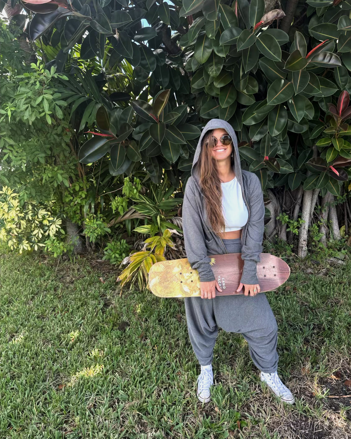 Person holding a skateboard in front of a green bush #color_grey