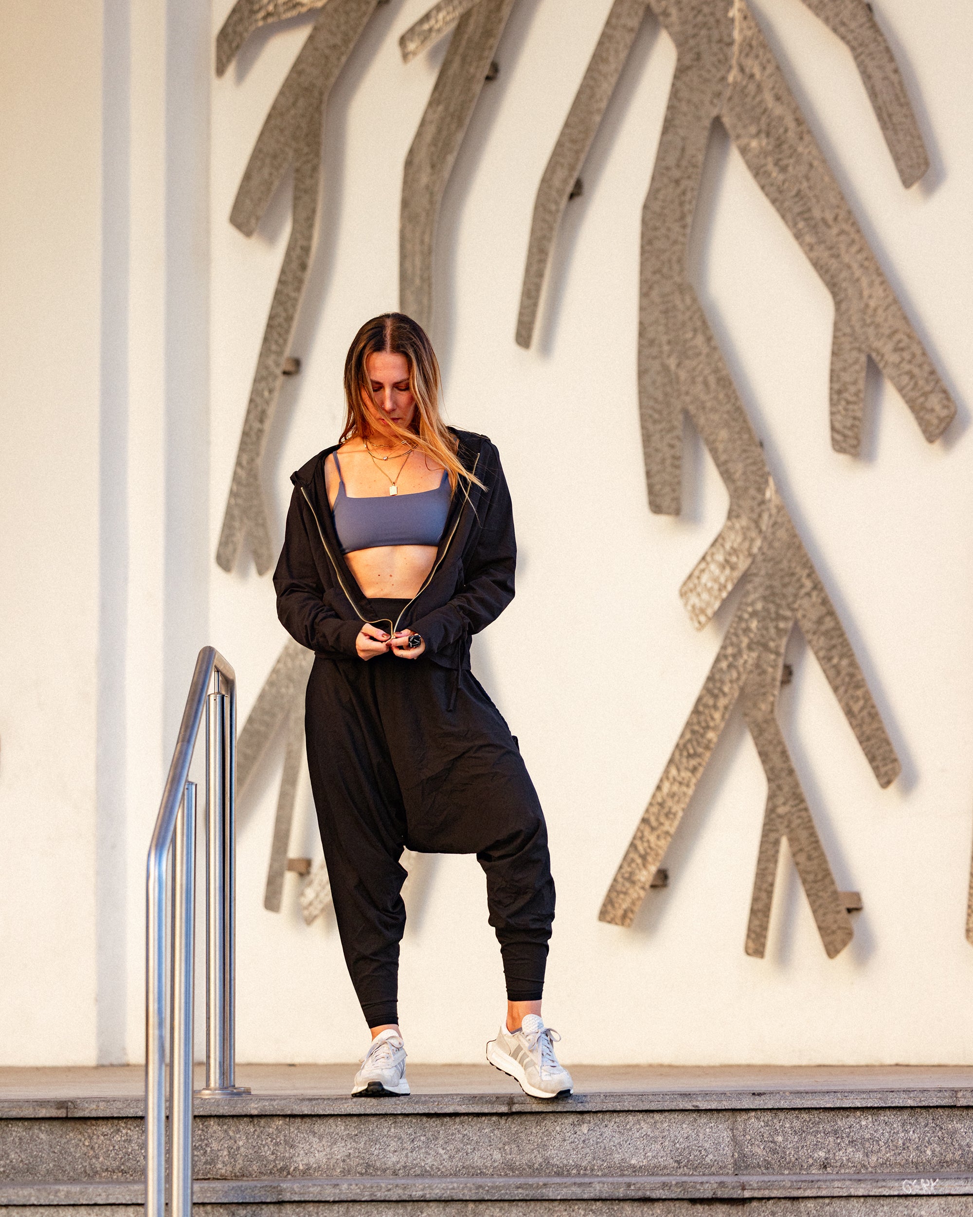 Woman in athletic wear standing on steps with decorative wall in the background #color_Black