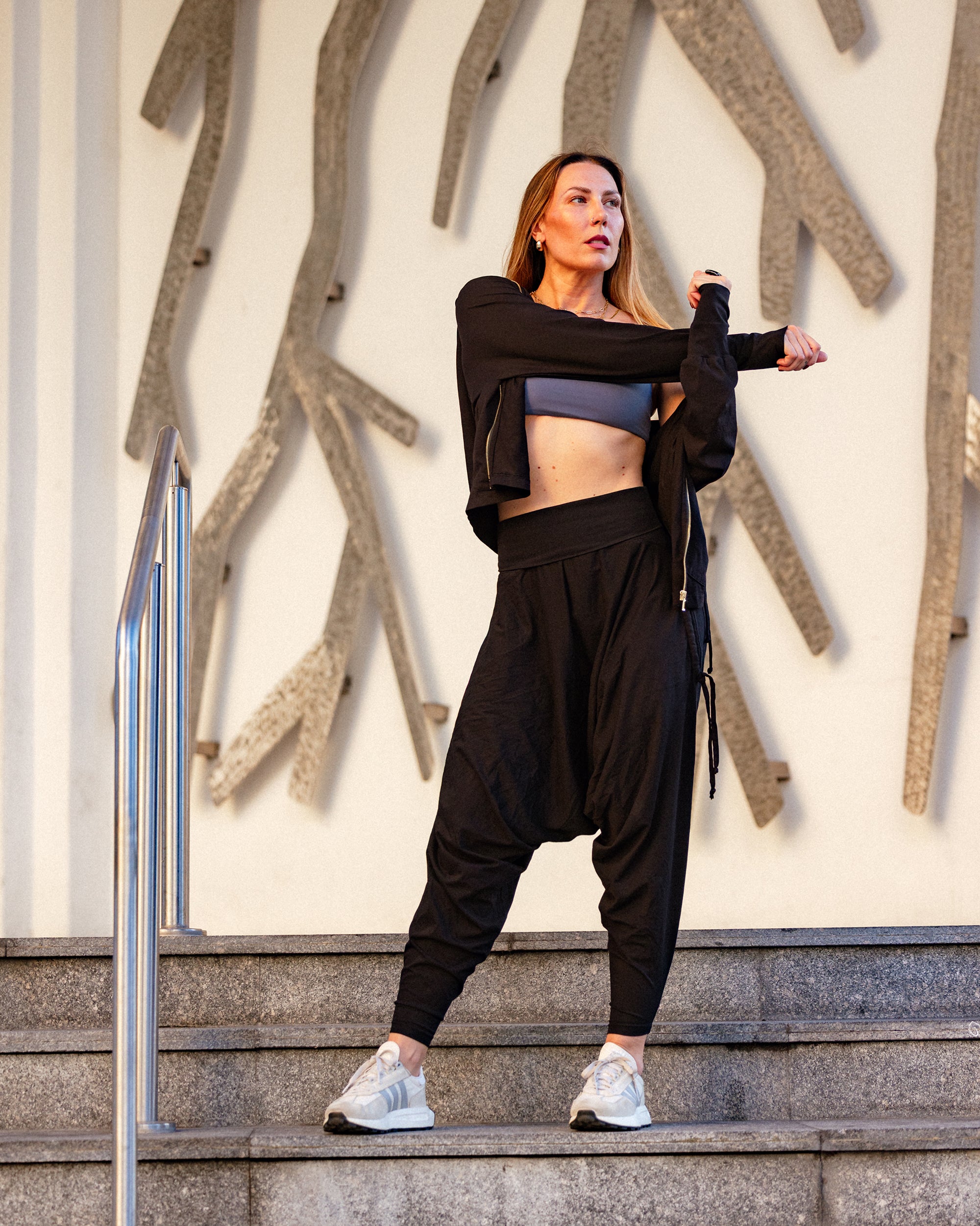 Woman in black athletic wear standing on steps with a textured wall background #color_Black