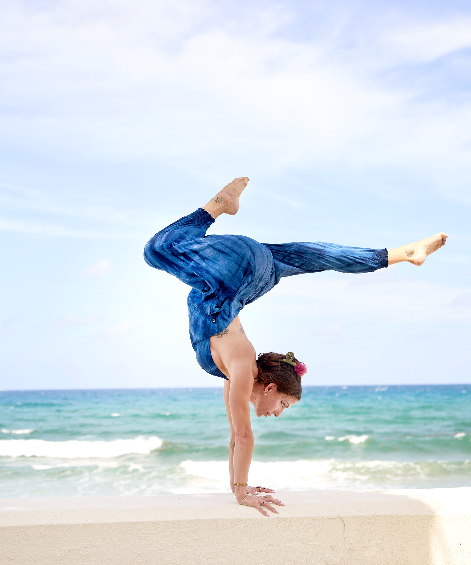 Woman in blue tie-dye jumpsuit doing a one-legged arm balance on the beach