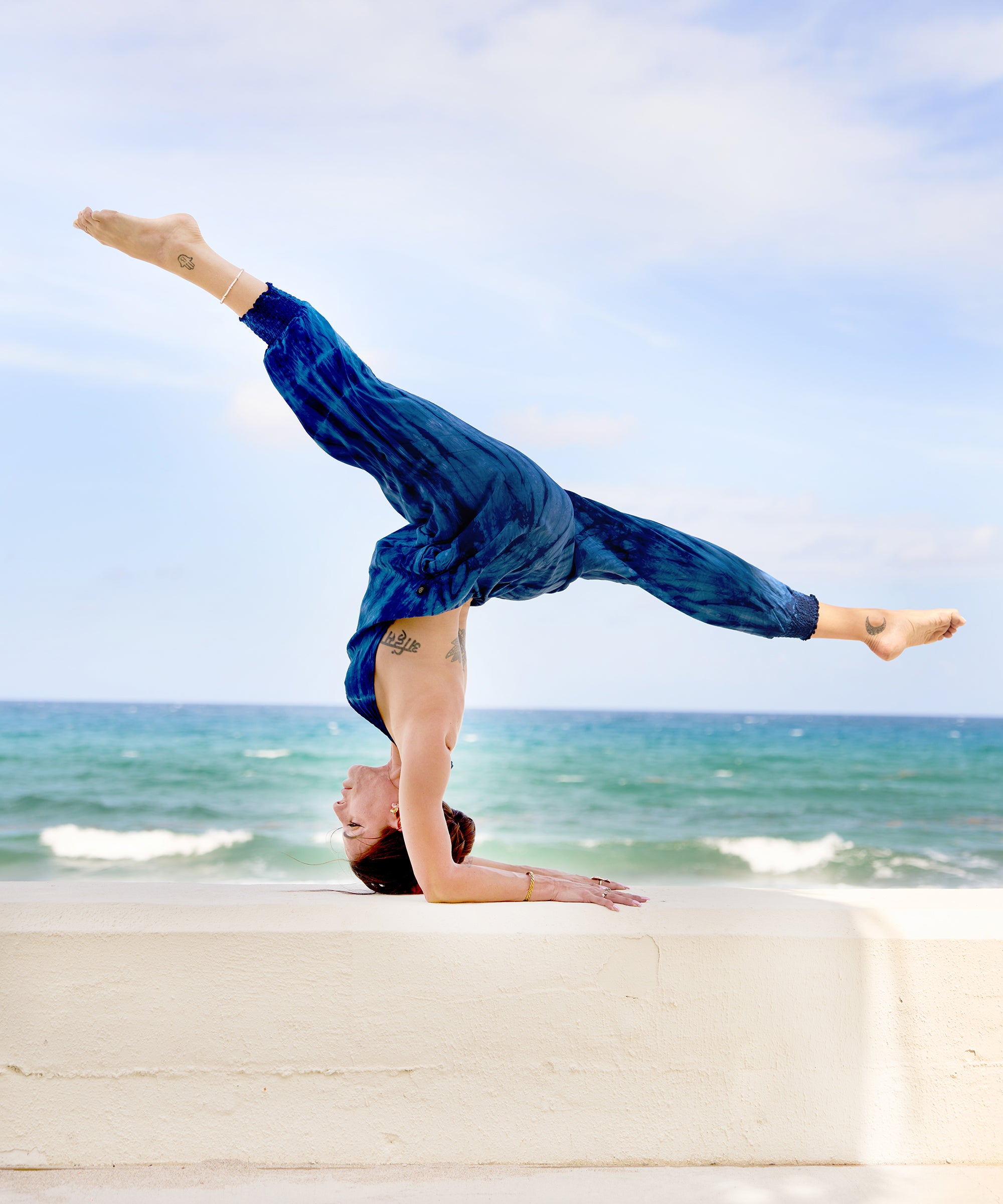 Woman in blue tie-dye jumpsuit in a beach handstand