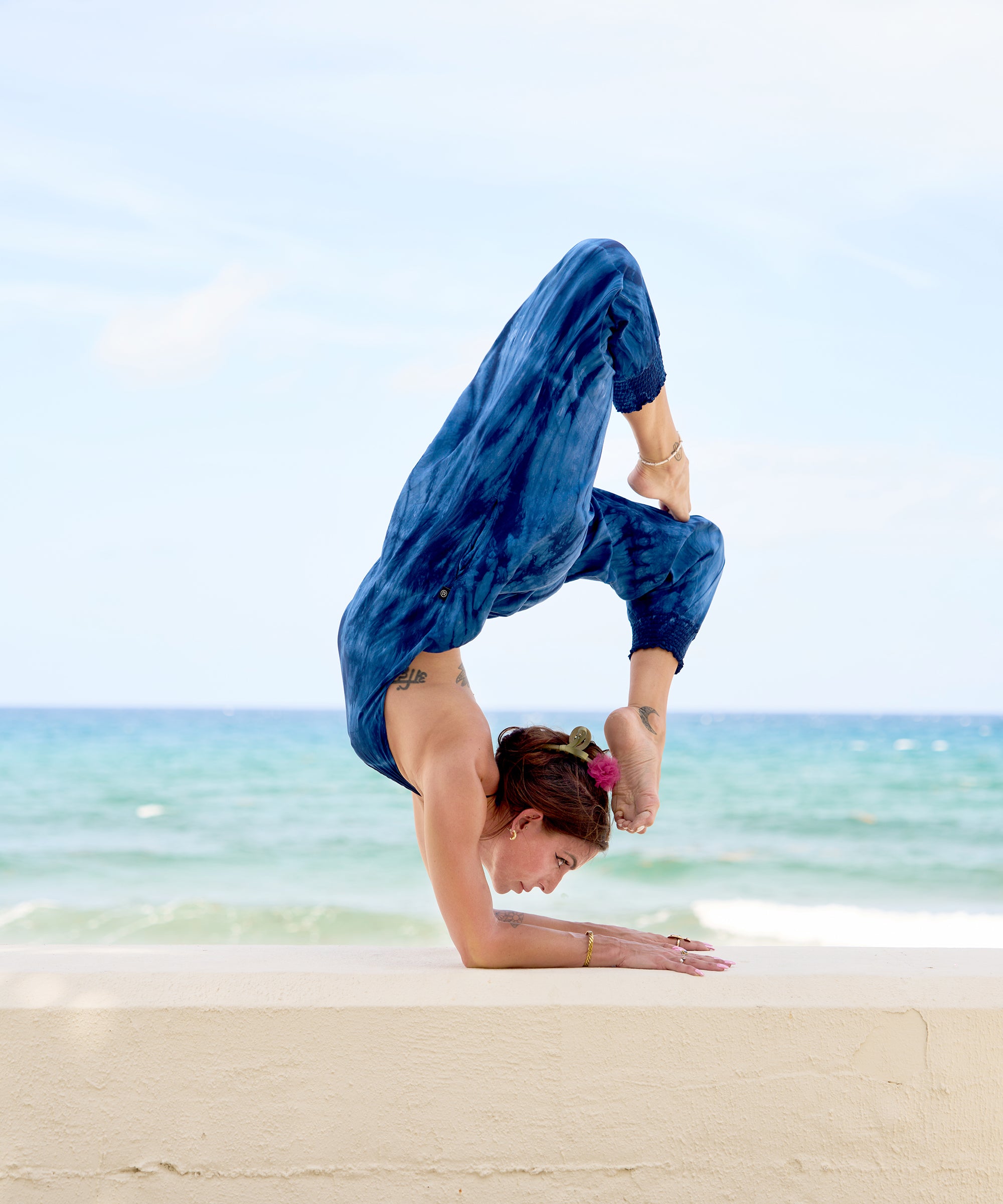 Woman in blue tie-dye jumpsuit doing a forearm stand on the sand
