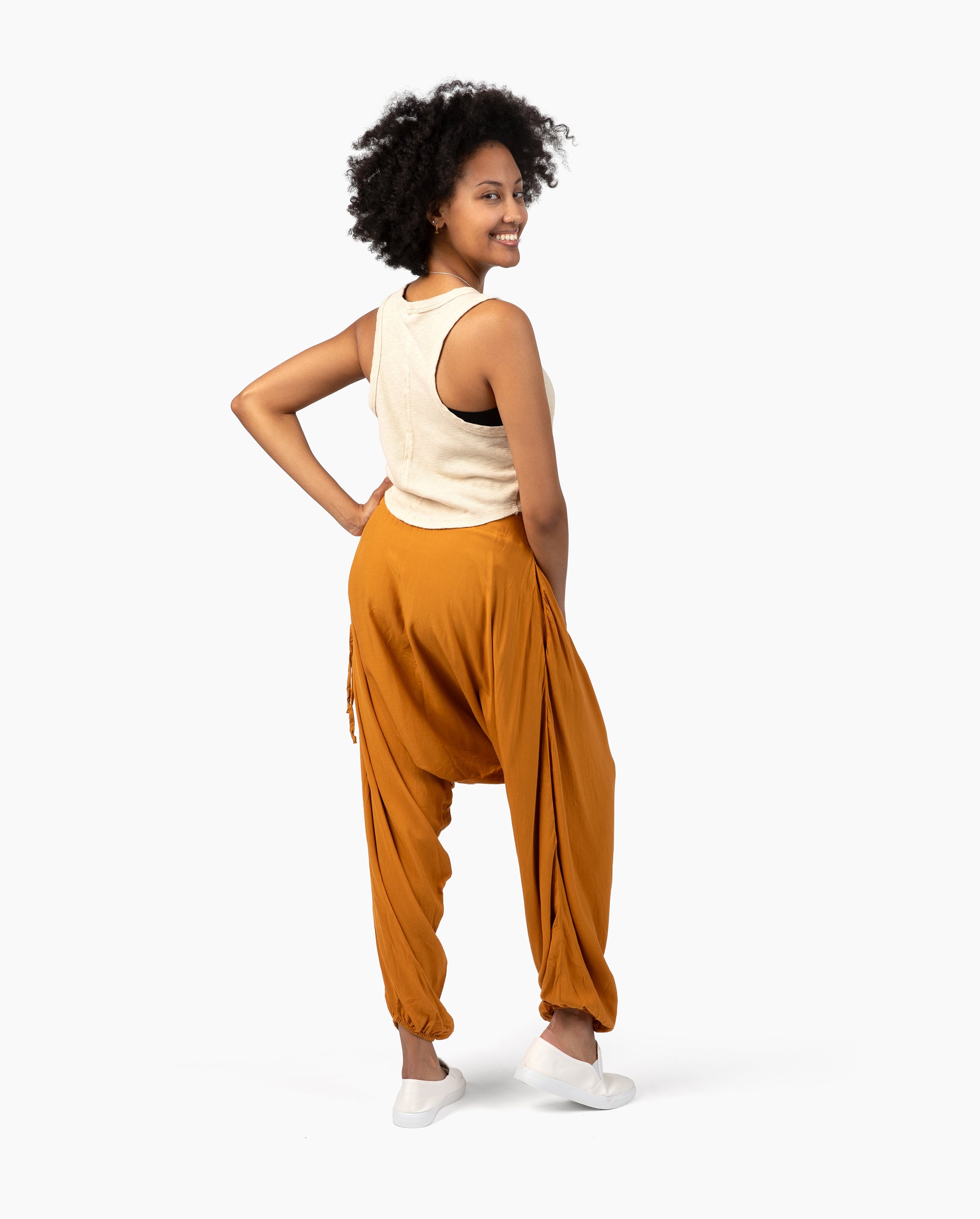 Woman wearing mustard-colored harem pants and a beige top on a white background #color_amber
