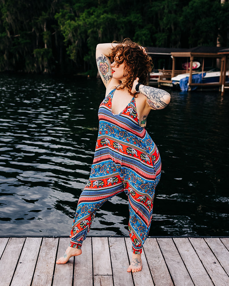 Woman wearing Savannah Flair jumpsuit in red elephant print, dancing on a dock #color_red elephant