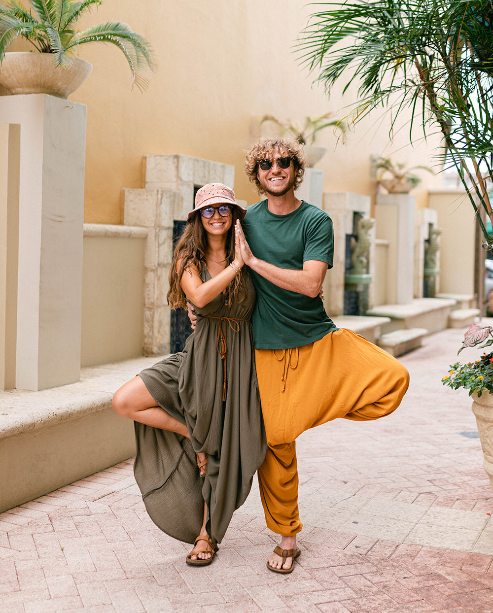 Two people posing outdoors with plants and architectural elements in the background #color_amber