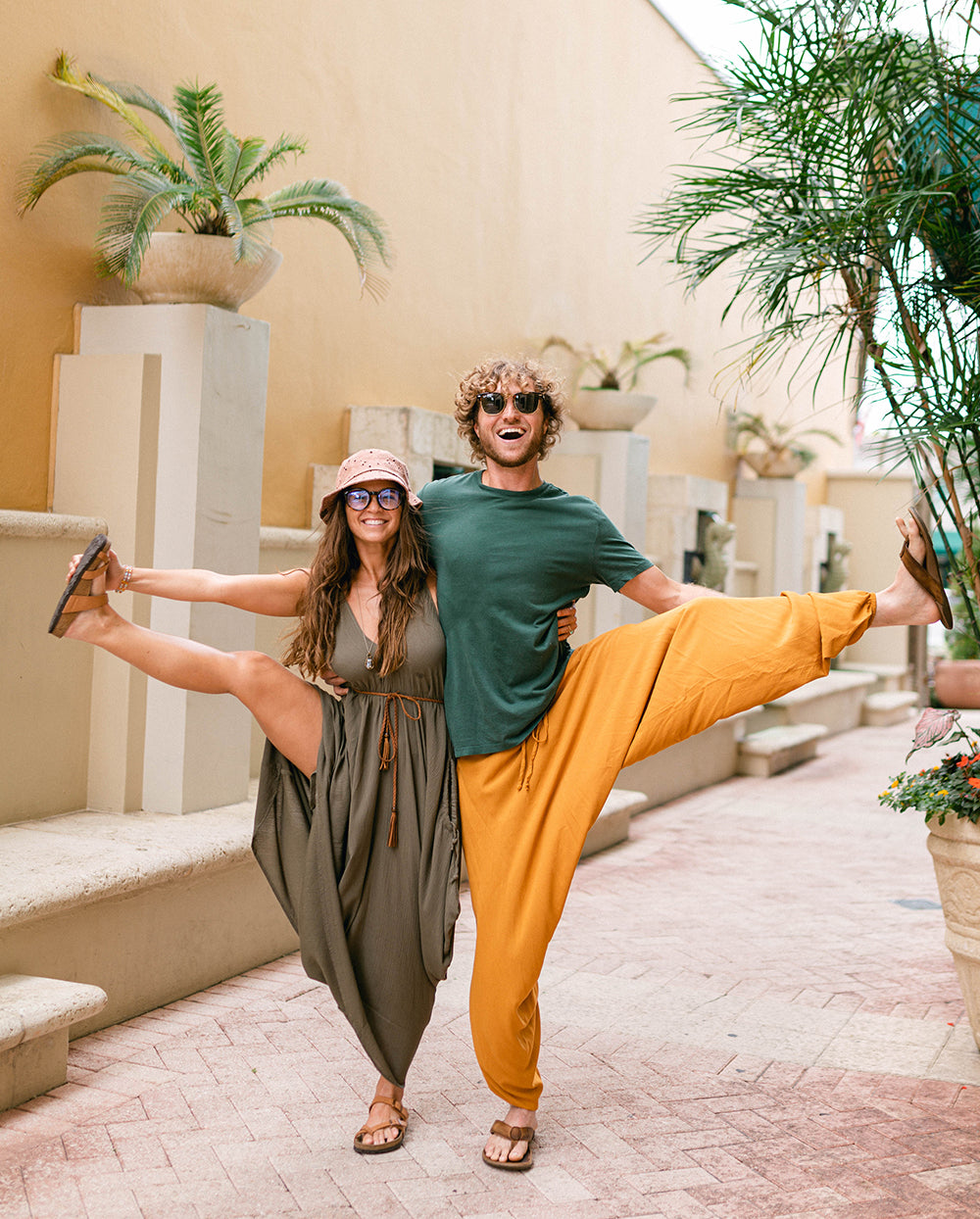 Two people posing with one leg up in a courtyard with plants and stone steps. #color_amber