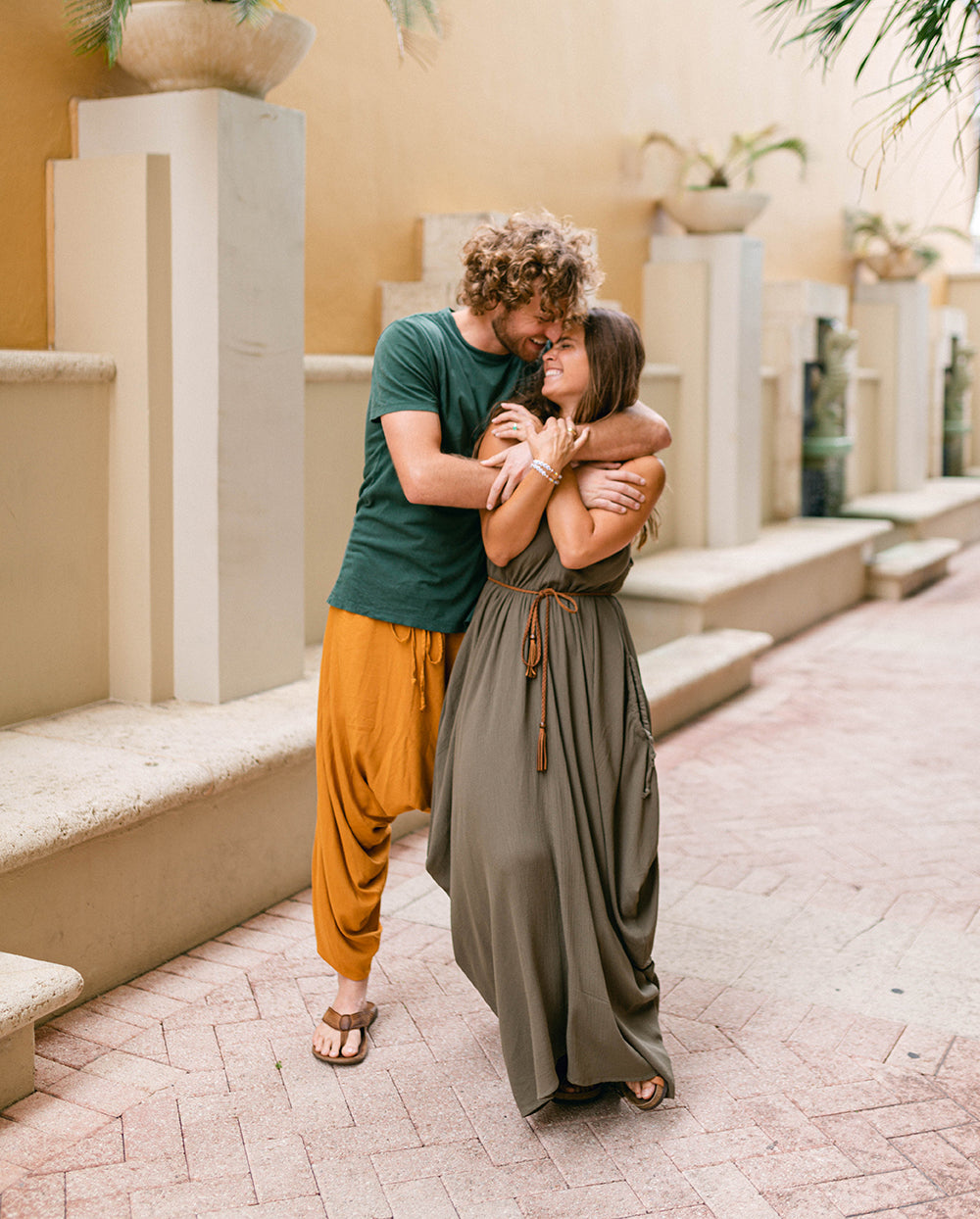 Couple embracing in a decorative outdoor setting with columns and plants. #color_basil
