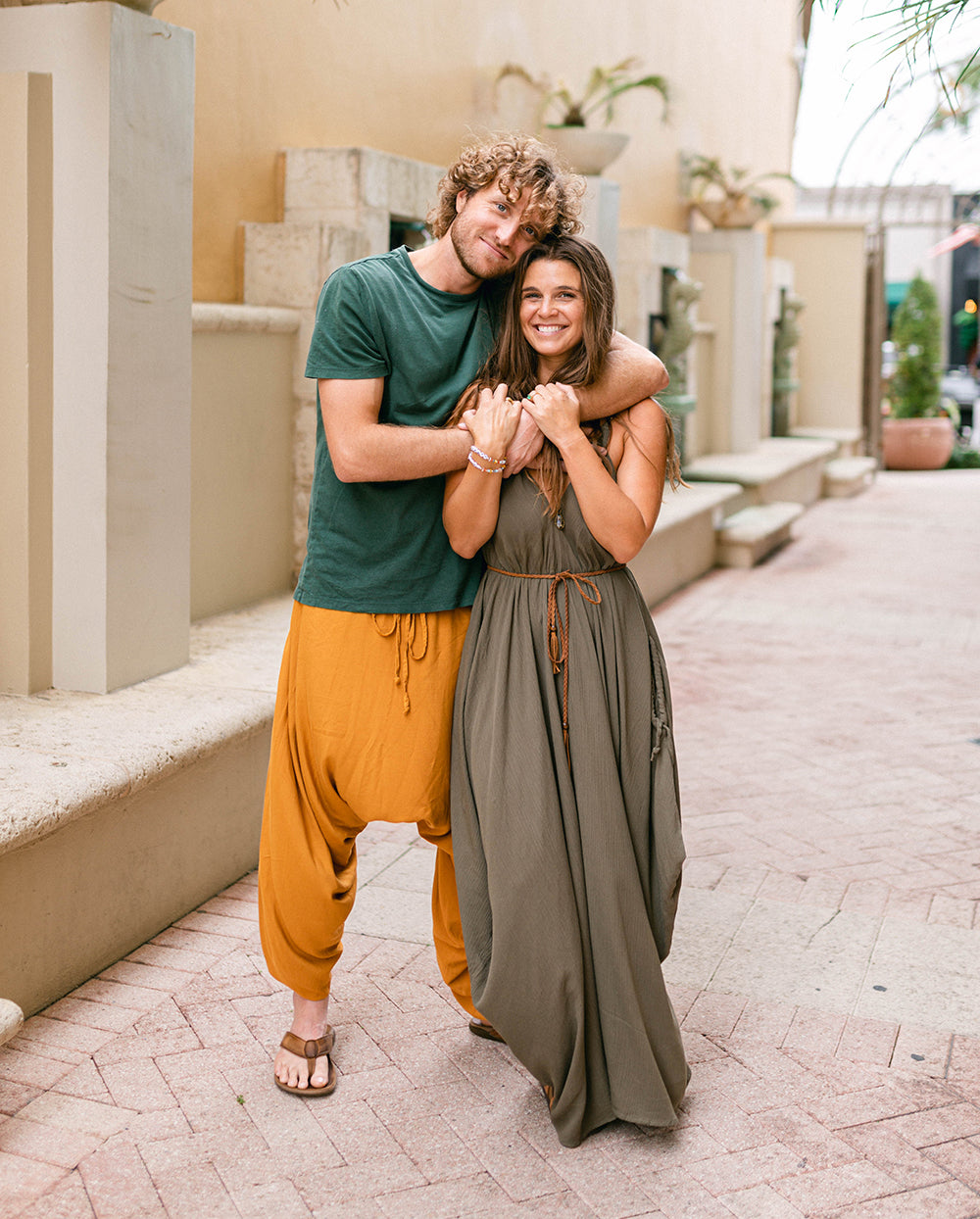 Two people embracing outdoors on a paved area with decorative columns and plants in the background. #color_amber