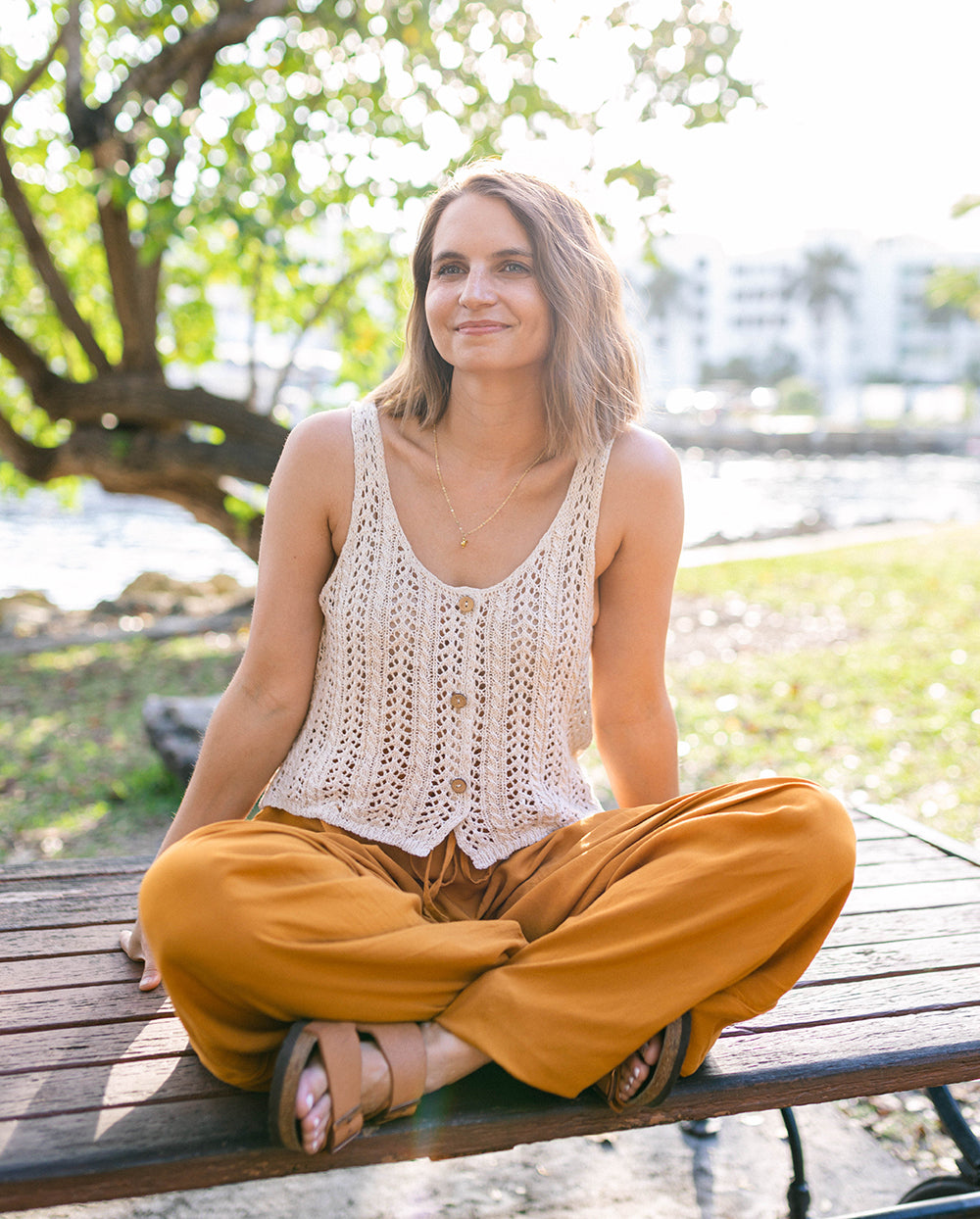 Woman sitting on a wooden bench outdoors with greenery in the background #color_amber
