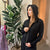 Woman wearing a black hoodie in a room with a plant and dresses in the background #color_black