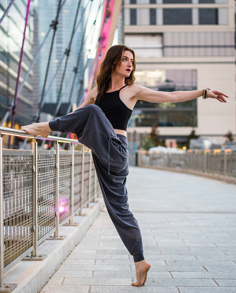 Dancer in a black top and gray pants performing on a city street with modern buildings in the background. #color_grey