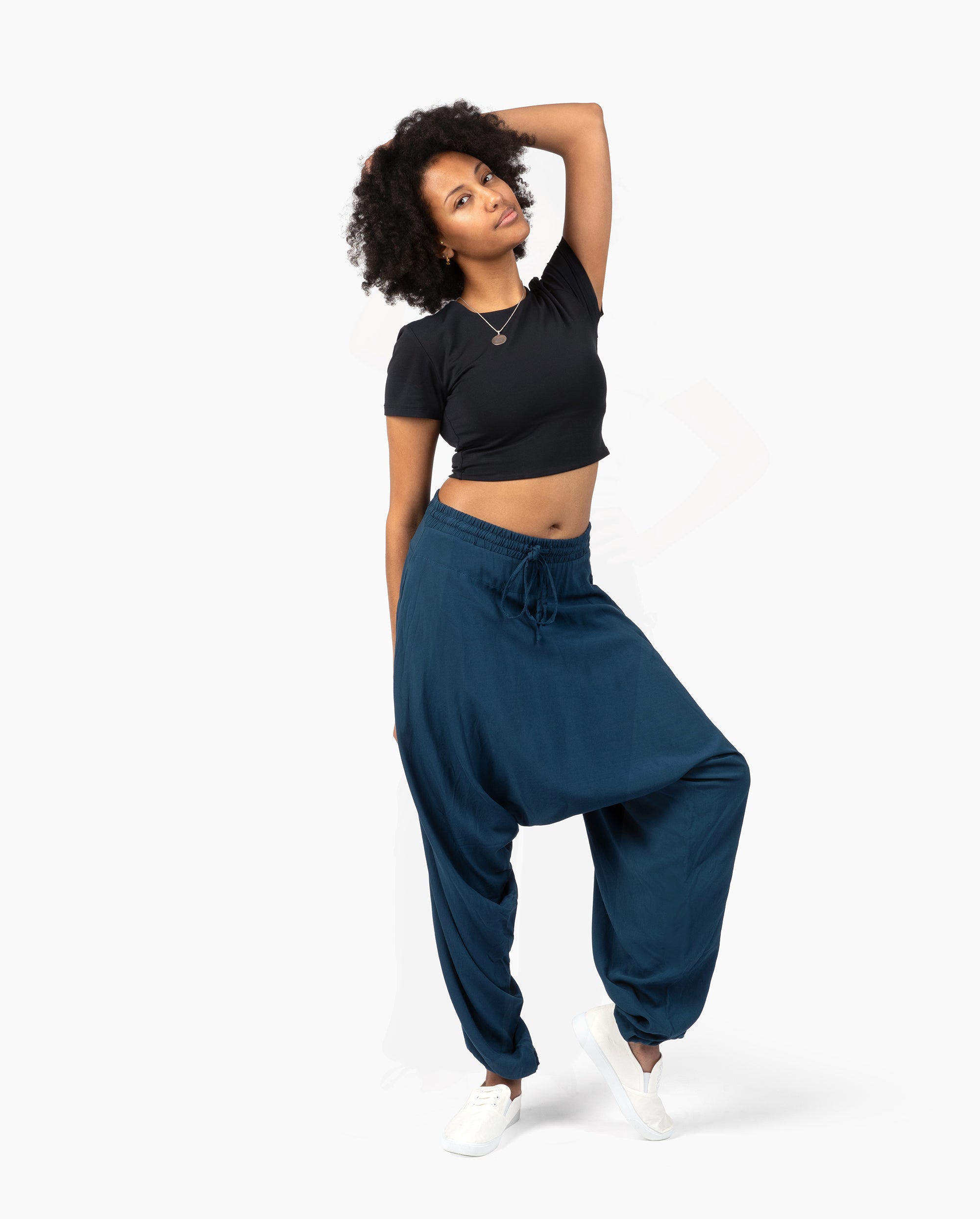 A woman posing in a black short-sleeve crop top and dark teal blue baggy sweatpants against a plain white studio background. #color_marine