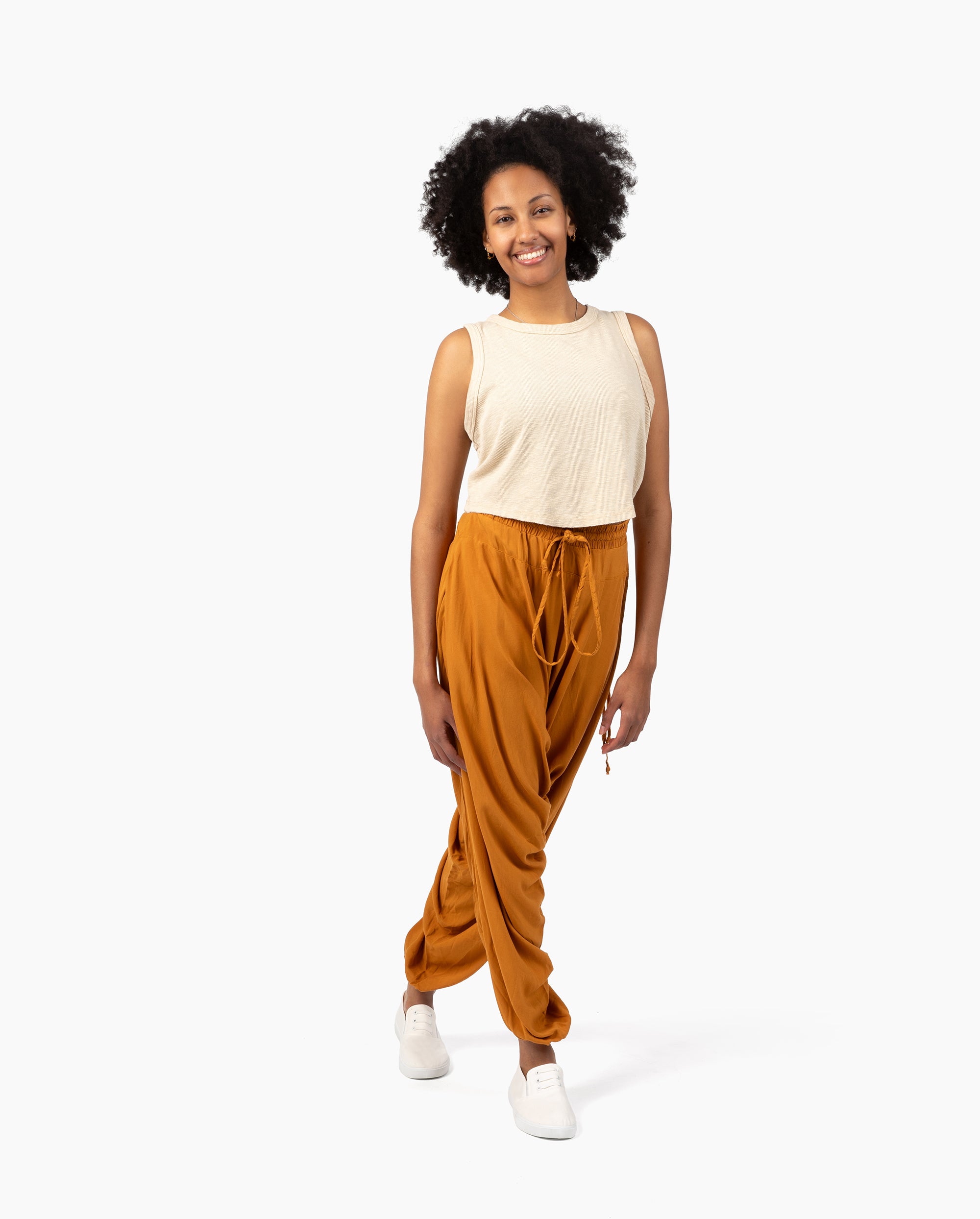 Woman wearing a beige sleeveless top and rust-colored harem pants on a white background #color_amber