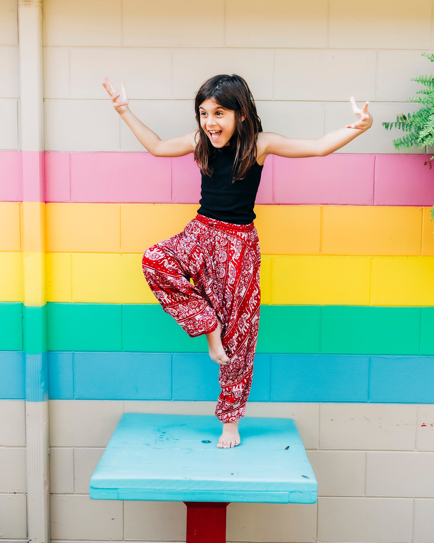 Child wearing red lotus yoga pants in front of colorful mural #color_red lotus